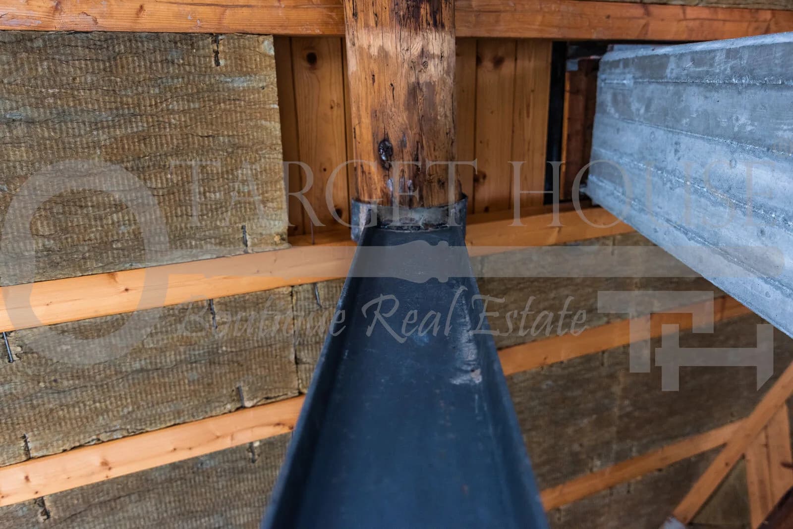 Interior roof structure of historic villa near Como showing wooden beams, rock wool insulation, and black metal guttering