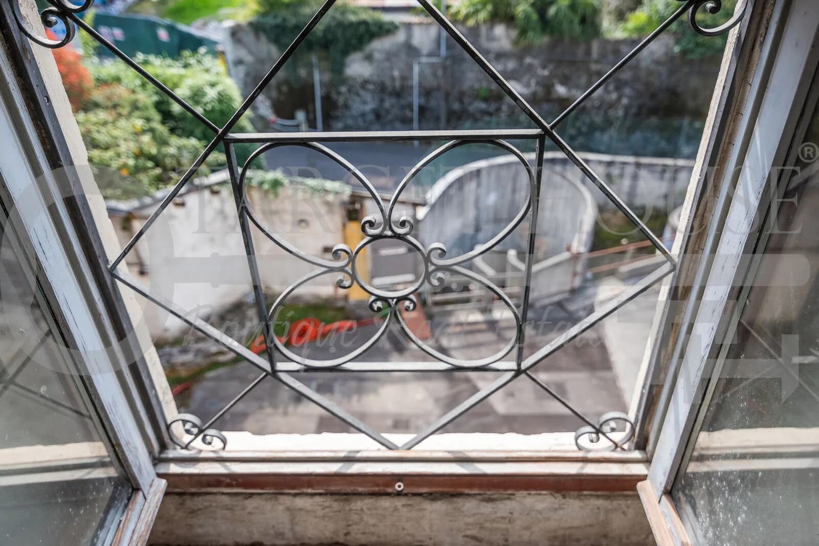 Ornate wrought iron window grate with floral scrollwork overlooking the courtyard garden of a historic villa near Como