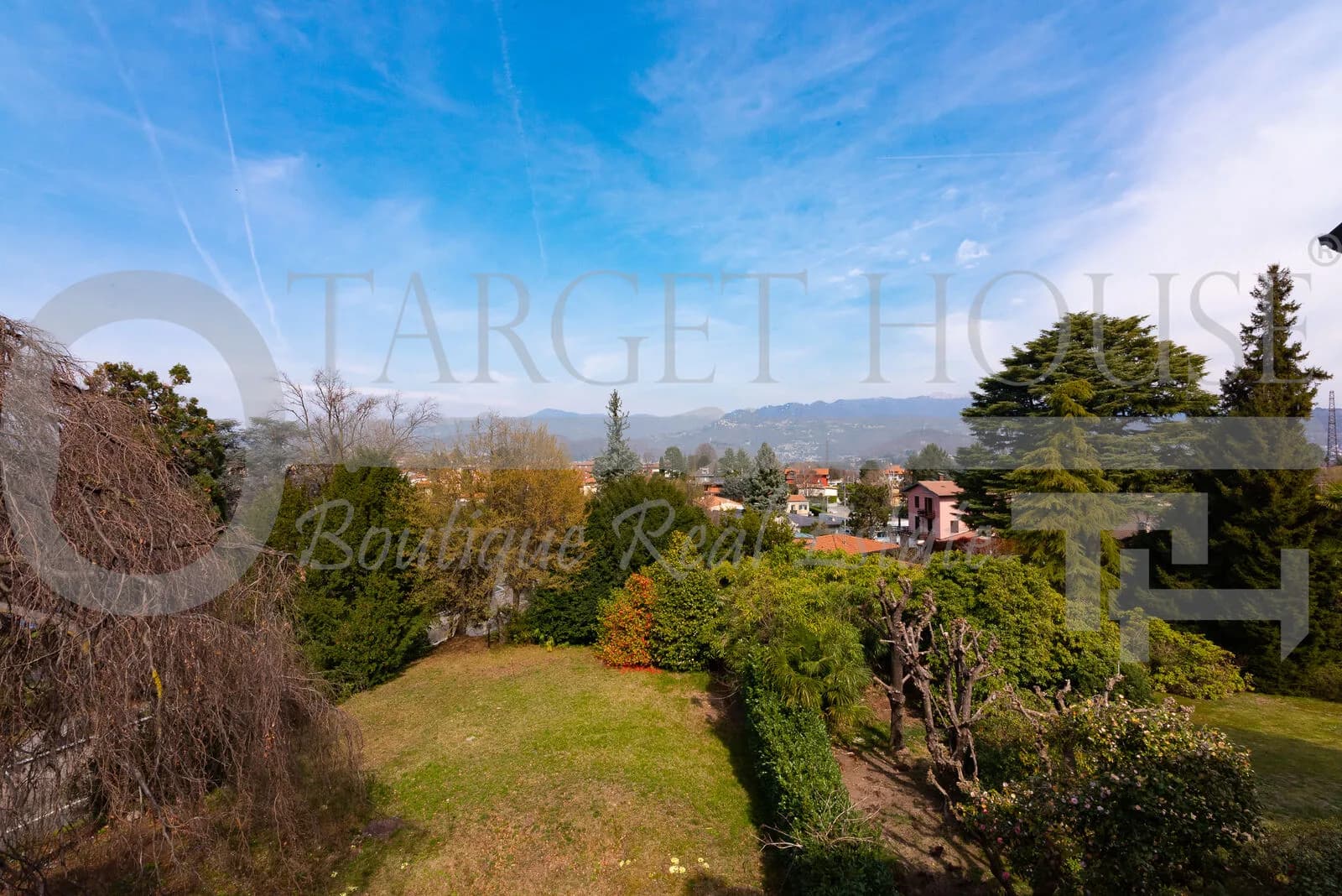 Lush 1,500 sqm garden with panoramic mountain views at historic villa near Como under a bright blue sky