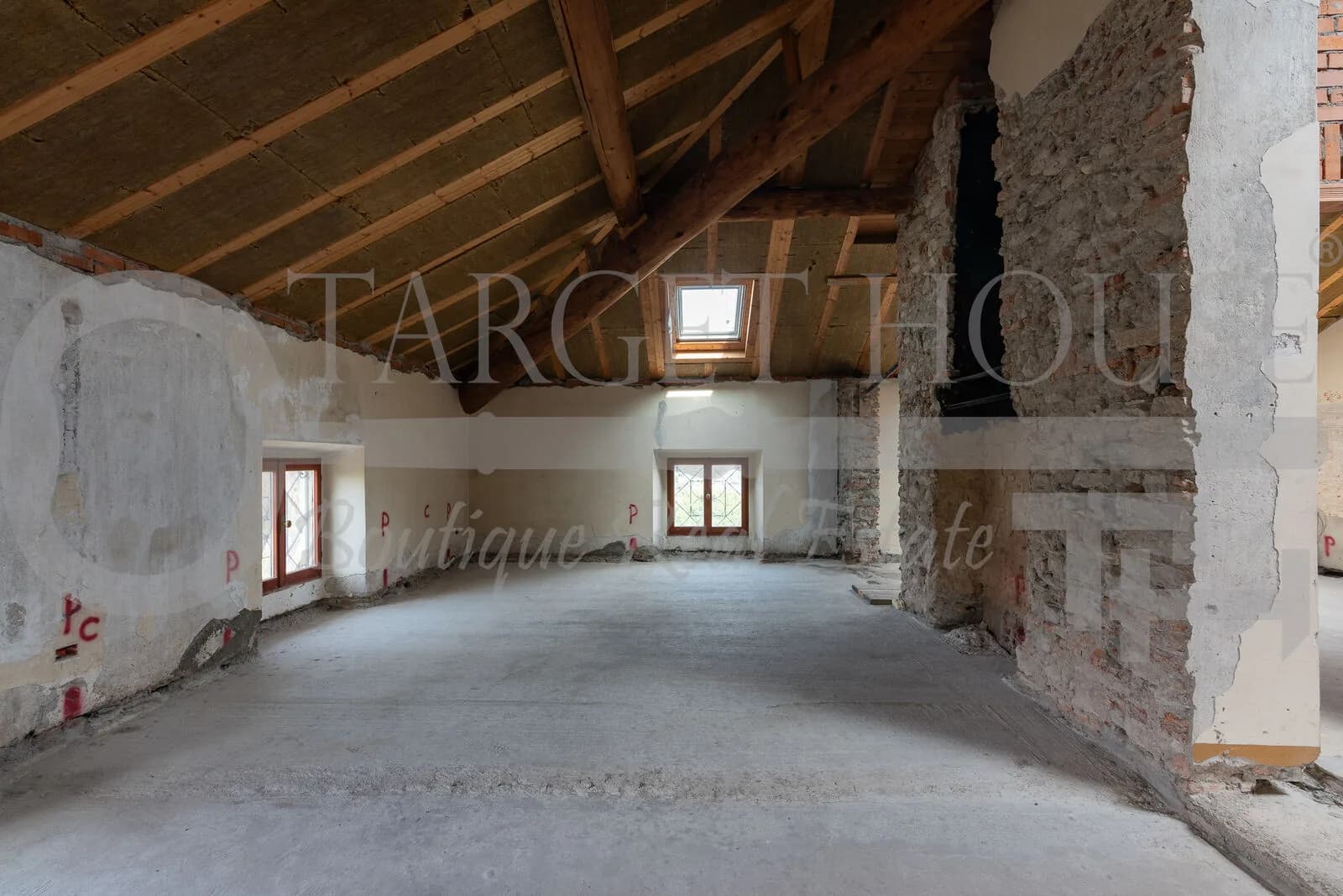 Unfinished attic space with exposed wooden roof trusses, skylight, stone walls, and concrete floor in historic villa near Como