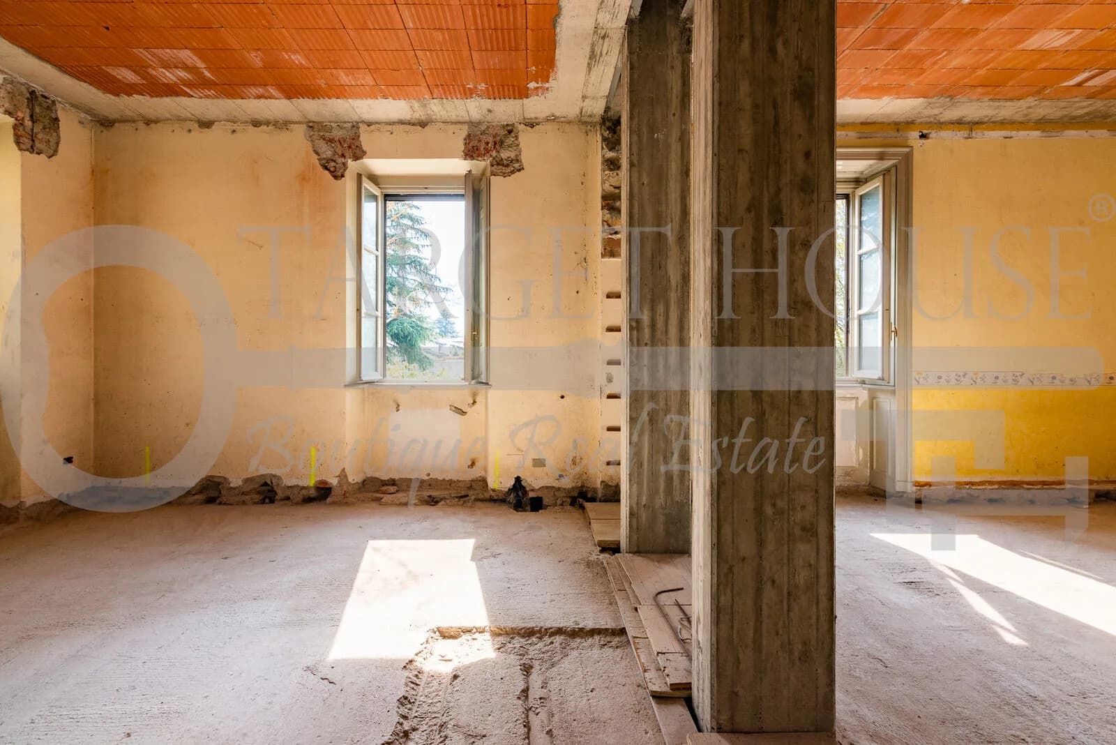 Bare concrete interior of historic villa near Como mid-renovation, exposed brick ceiling, raw walls, two open windows