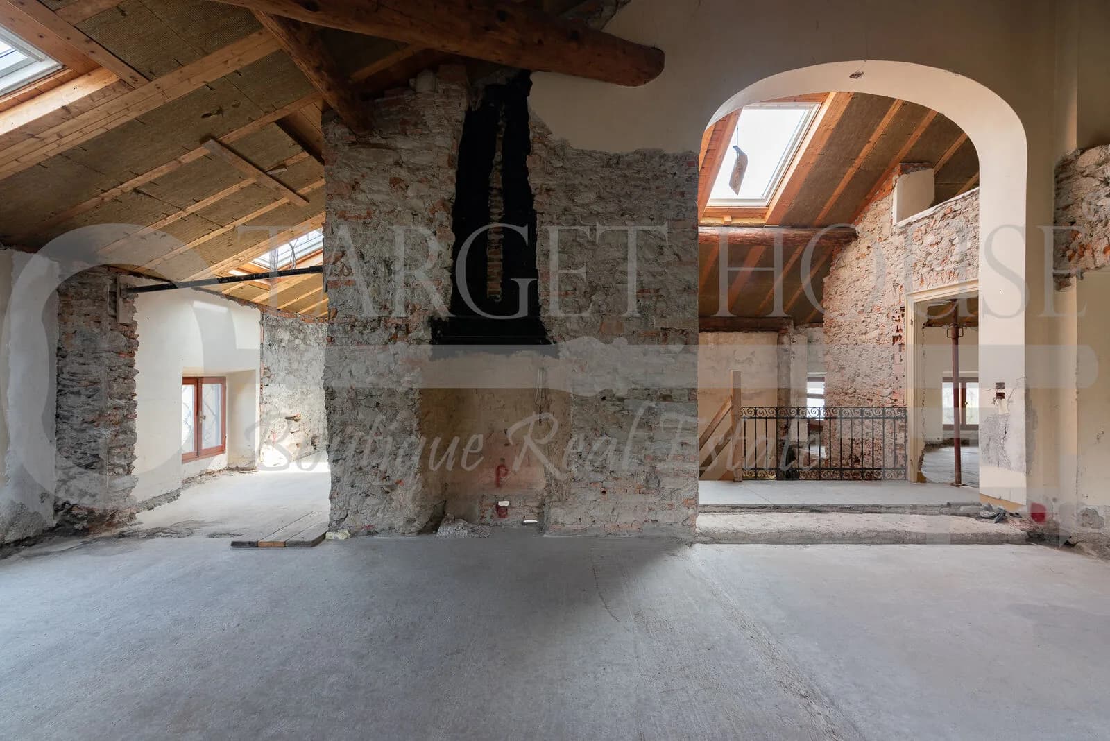 Unfinished attic interior of historic villa near Como with exposed brick walls, wooden roof beams, and skylight windows