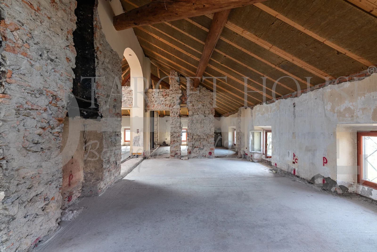 Unfinished attic interior of historic villa near Como with exposed stone walls, wooden beam roof, and arched doorway
