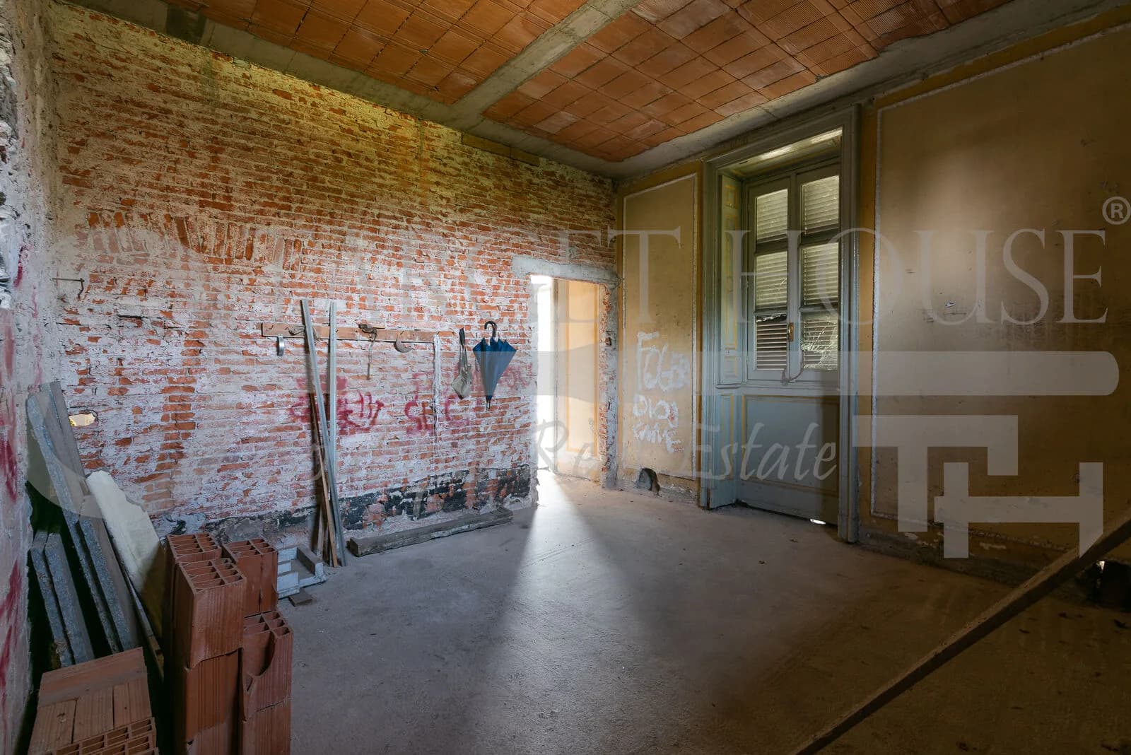 Bare brick interior room with exposed walls, terracotta ceiling, concrete floor, and original shuttered windows in historic villa near Como