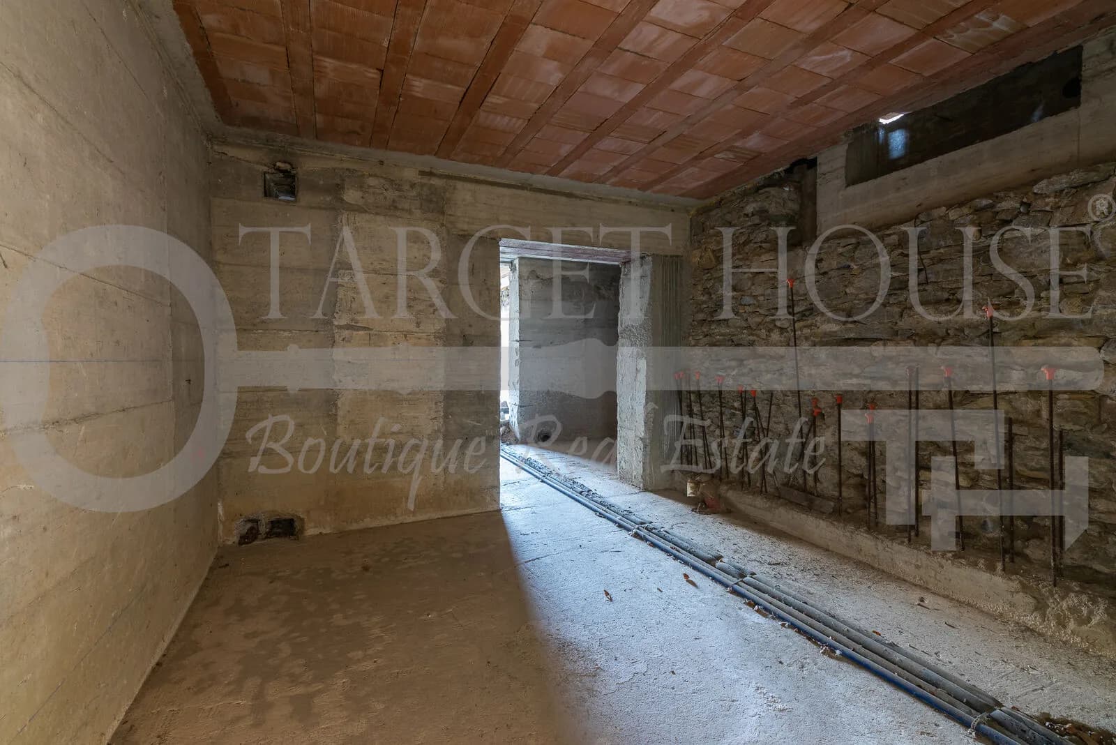 Unfinished stone interior room with terracotta ceiling, exposed conduit pipes, and doorway opening — historic villa near Como renovation
